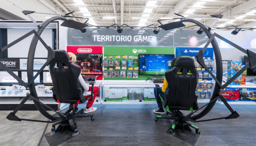 Foto con dos personas sentadas en asientos para gamers, frente a tienda de Nintendo y Xbox